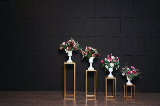 golden iron racks with a white flowerpot with artificial flowers on a black background. white pot with flowers on the background of black walls in a photo studio. gothic style wedding photo zone