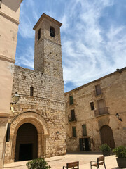 Fototapeta na wymiar Montblanc, Spain, June 2019 - A stone church with a clock tower in front of a brick building