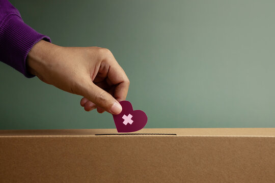 Donation Concept. Hand Drop a Paper Heart with Cross into a Donate Box. Helping, Supporting and Togetherness. Side View