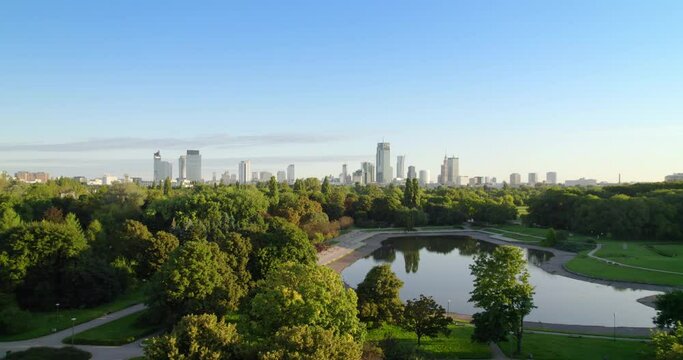City park with the city center in the background. Aerial view of offices in skyscrapers over the panorama of Warsaw in a urban park. Lake in the park with green trees during summer.
