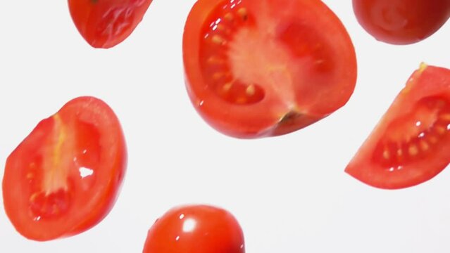 Fresh ripe tomato halves are falling diagonally and rotating on white background