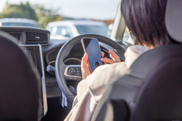 運転席でスマートフォンを操作する女性
