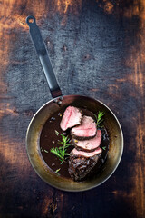 Traditional German venison roast with juniper berry and rosemary in spicy red wine sauce served as top view in a frying pan - obrazy, fototapety, plakaty