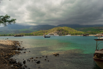 A bay with ships, mountains, clouds, clear blue water and rocks