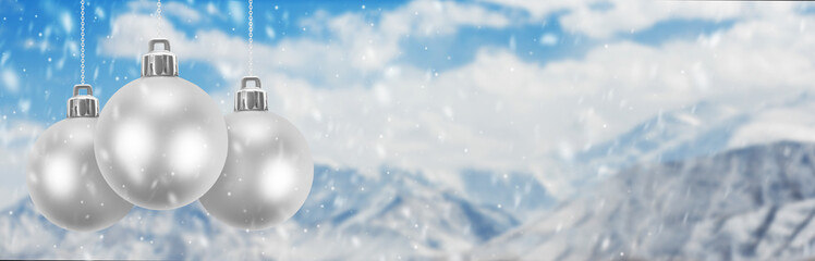 Three silver Christmas balls against the backdrop of a mountainous snowy landscape.