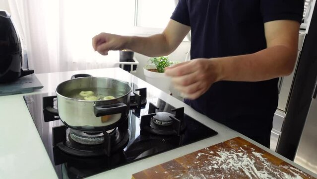 Chef cook hand making handmade tortellini ravioli with boiling water in pot saucepan on stove fire.