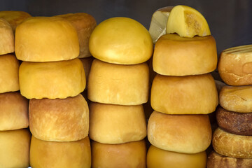 Cheese heads of different colors and sizes are stacked on counter. Fair trade in homemade cheese. Close-up. Selective focus.