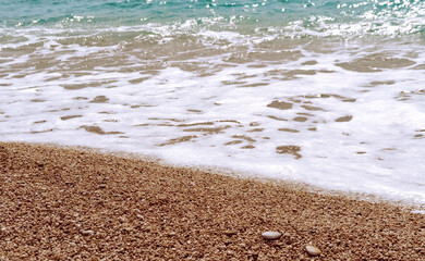 Fototapeta na wymiar Sea foam on the pebble shore beach on sunny day