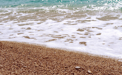 Sea foam on the pebble shore beach on sunny day