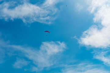 Naklejka na ściany i meble paragliding pilot flying high in the blue sky with clouds
