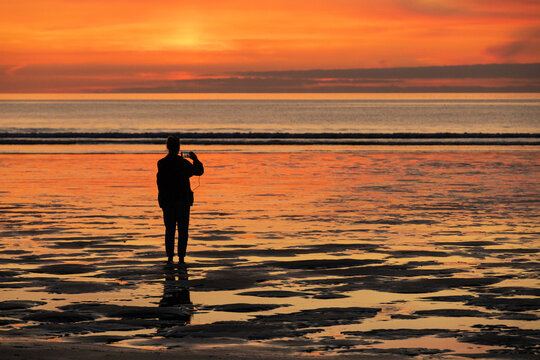 silhouette of a person on the beach at sunset taking photo