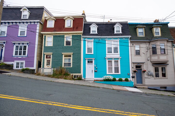 Brightly colored wooden row houses with a blue sky in the background. The three story houses are colorful with multiple casement windows and flat roofs.  