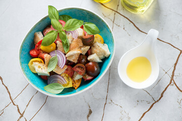 Bowl with panzanella or italian tomato and bread salad, high angle view on a light-beige marble background, horizontal shot