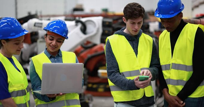 Multiracial engineers working inside robotic factory using computer laptop and mobile phone