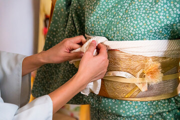 Japanese, Okinawan woman's hands tying obiage cloth around the obi during traditional kimono dressing
