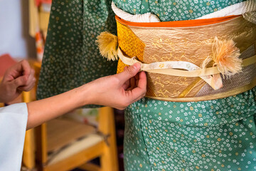 Japanese, Okinawan woman's hands adjusting obijime belt around the obi during traditional kimono...