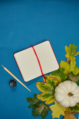 Notebook with ink pen, leafs and pumpkin on blue background