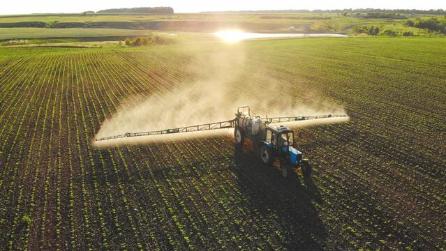 Aerial view of working farming tractor spraying on field with sprayer water or herbicides and pesticides against diseases and insects. Nature landscape of rivers, reservoirs. Agricultural industry.