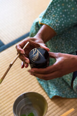 African American woman guest hands holding chashaku bamboo matcha tea spoon and Natsume lacquered...