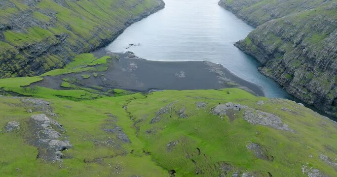 Aerial Descending Tilt Up Shot Of Sea Amidst Natural Green Mountains - Faroe Islands, Denmark