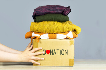 closeup woman hands holding carton box with used clothes for donation, collection and support of...