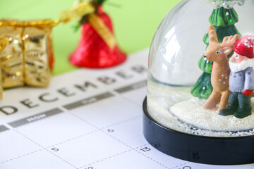 Christmas time concept, close up of festive snow globe on December calendar, Christmas present and bell in background, selective focus