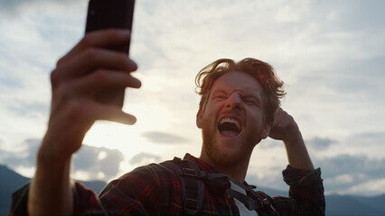 Closeup excited blogger take selfie on phone. Hipster reach peak on mountains.