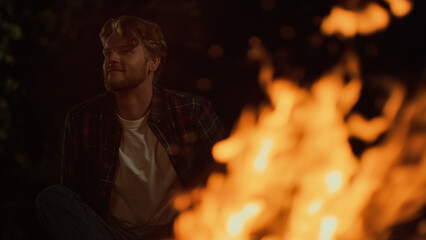 Obraz premium Closeup smiling camper enjoy bonfire on dark night. Cheerful man sit in forest.