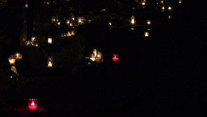 All Saints Day. Candles burn on graves at cemetery at night. All Hallows Eve / Day of All the Saints / Solemnity of All Saints / 1st November / Happy Halloween. Zoom out shot. 4K
