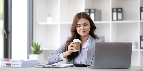 Young woman working on a laptop in the office. Asian businesswoman sitting at her workplace in the office. Beautiful Freelancer Woman working online at her home.