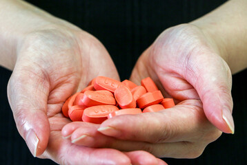 Holding a pile of red tablet capsule pills in the palm of hands, health and medicine concept