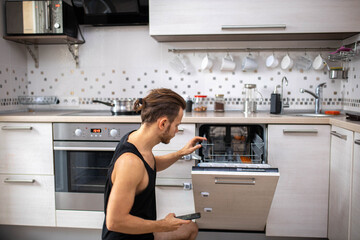 man in the kitchen studies the instructions for a dishwasher in a smartphone.