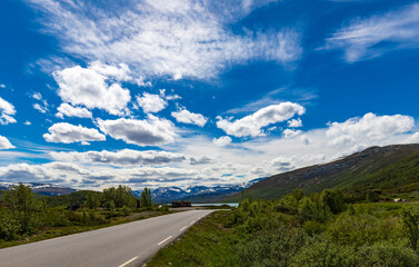 Scandinavian Summer Afternoon With Road And Snow Capped Mountains In The Distance Under Blue Skies In Norway June 2019