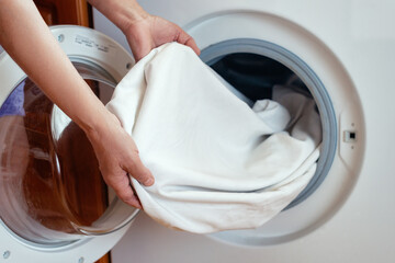 Close-up of women's hands pulling clean white linen clothes out of the washing machine after washing in the bathroom.Women's hands put the laundry in the washing machine.Routine homework.Laundry day.