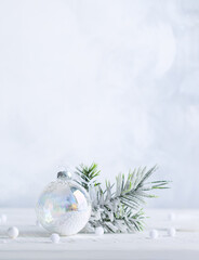 Christmas minimalist still life with snowy fir branches and transparent Christmas ball on light background. Winter or Christmas festive concept.