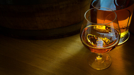 a glass of luxury alcoholic drink, an oak barrel and a bottle of cognac on a dark background