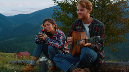 Music couple sit camp in mountain landscape. Carefree lovers play guitar outside