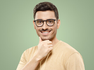 Handsome positive guy wearing beige t-shirt and eyeglasses, touching his chin making decision