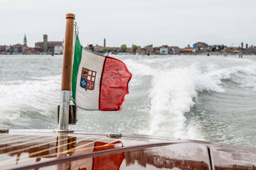 The Venetian flag, flying from the back of a water taxi, on the Venetian lagoon - obrazy, fototapety, plakaty