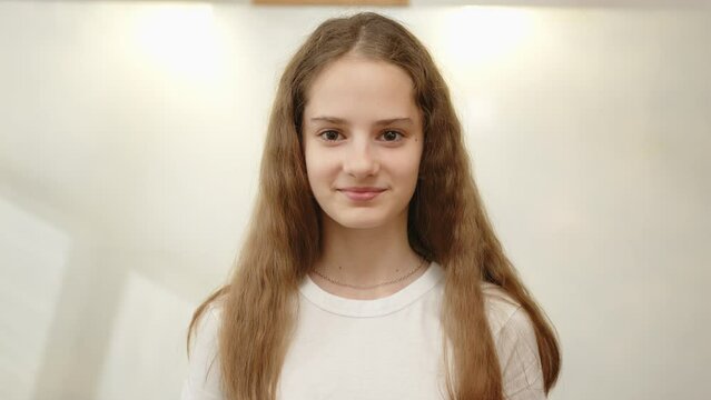 Portrait of young girl 12 years old with long hair smiling looking at camera indoors close-up.
