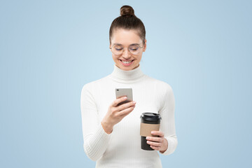 Young attractive woman wearing eyeglasses and white turtleneck, holding phone and coffee cup