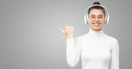 Horiozntal shot of girl in headphones and white turtleneck, pointing at copy space on left, smiling