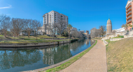 Pathway at River Walk with a view of reflective San Antonio River and residential buildings- Texas
