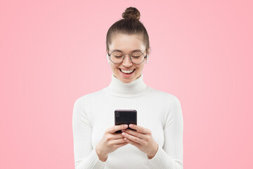 Young female in round glasses feeling relaxed and happy, laughing at funny content on phone screen