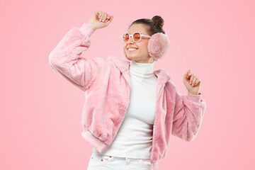 Active girl wearing pink fluffy coat, colored glasses and ear warmers, moving to sounds of music