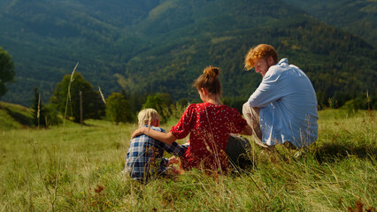 Fototapeta na wymiar Happy family relaxing sitting green hill. Parents enjoying holiday with kids.