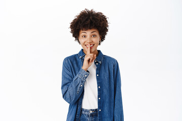 Portrait of Black woman shows hush, shhh shush gesture, taboo, asks to keep quiet, gossiping, stands over white background