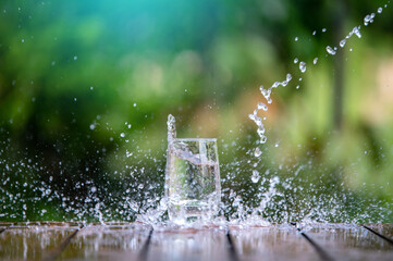 Drink water pouring in to glass over sunlight and natural green background.Water splash  in glass...