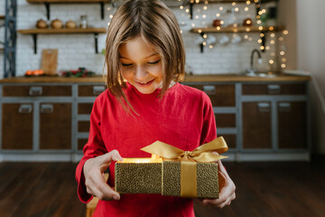 Girl wearing in red sweater opening golden gift box