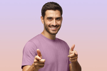 Young man in purple t-shirt pointing to camera with fingers isolated on purple background